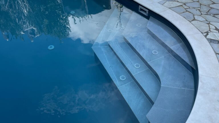 Ovalpool mit weißen Feinsteinzeugtrittplatten