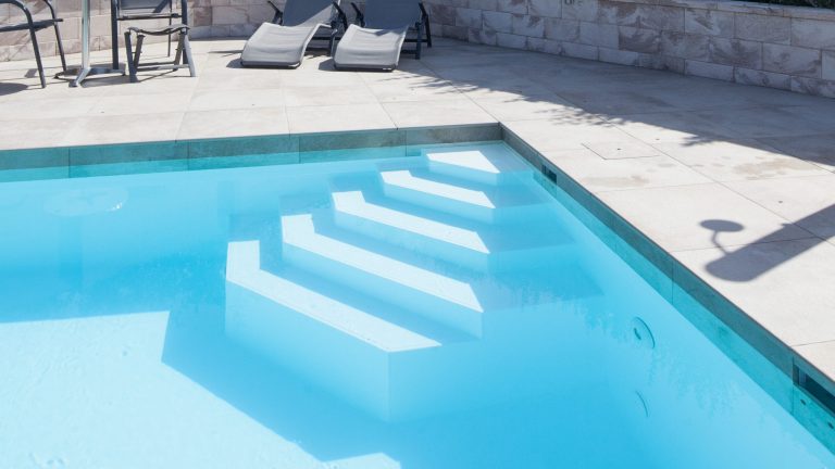 Poolrand-Gestaltung inkl. Vertikalstein bei Rechteckpool mit Ecktreppe und weißer Poolfolie - Happy-Pool".