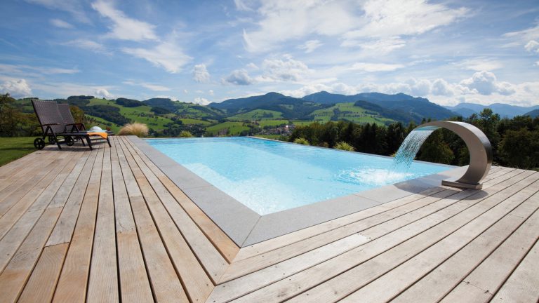 Pool mit Holzdeck und Wasserfall vor atemberaubender Bergkulisse